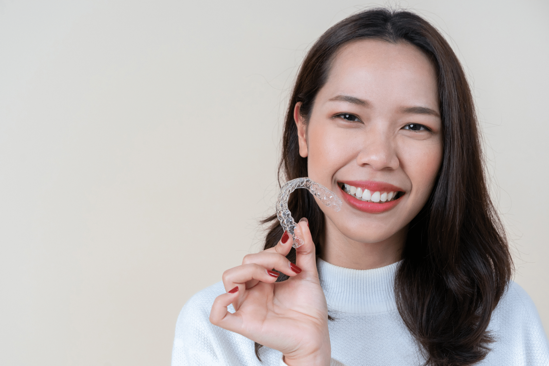 Smiling woman holding a clear aligner tray up near her face